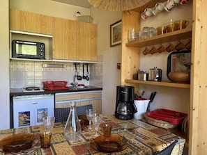 A compact kitchen with wooden cabinets, a microwave, a coffee maker, and a dining table set with glasses and plates. - 1st floor, view mountain, balcony, parking, tv, 20m², Montgenèvre (Montgenèvre)