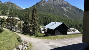 Une cabane de montagne avec un toit en métal, entourée d’arbres et sous un ciel dégagé.