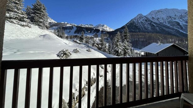 Un balcon offrant une vue sur un paysage montagneux enneigé, avec des arbres et un bâtiment.