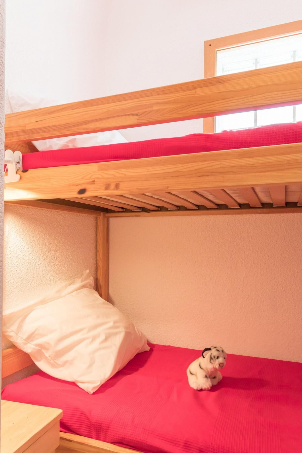 A bunk bed with a red mattress and a small dog toy on the lower bunk.