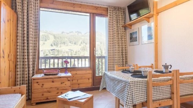 A wooden room with a bed, a small table, a dining table with chairs, and a window with a view of a forested mountain. - 2nd floor, view mountain, balcony, parking, tv, 20m², Montgenèvre (Montgenèvre)