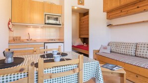 A compact kitchen with wooden cabinets, a microwave, and a sink. There is a dining table with chairs and a checkered tablecloth. A wooden sofa with a plaid cover is in the living area. - 2nd floor, view mountain, balcony, parking, tv, 20m², Montgenèvre (Montgenèvre)