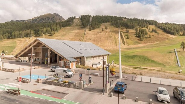 Ein Gebäude mit geneigtem Dach, einem Parkplatz und Blick auf eine hügelige Landschaft.