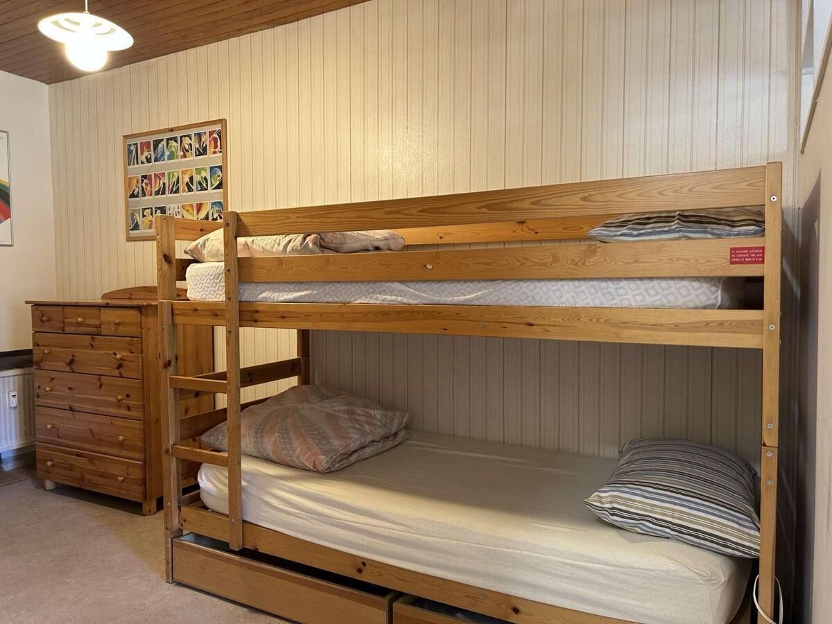 Una cama litera con estructura de madera, un aparador y un cuadro colgado en la pared.