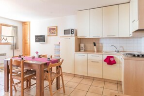 Een kleine keuken met een eettafel, stoelen, een magnetron, koffiezetapparaat en een fornuis.
