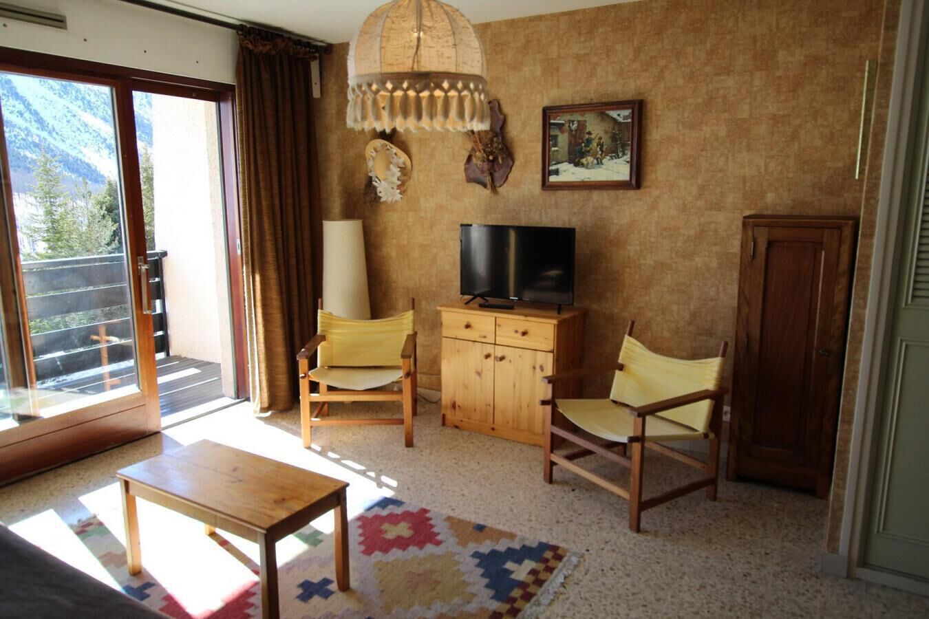 Un salon chaleureux avec un meuble en bois, deux fauteuils jaunes, un téléviseur et un tapis coloré.