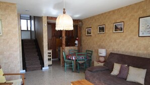Una sala de estar con un sofá, una mesa de centro de madera, una mesa de comedor con sillas, una lámpara colgante y una escalera que lleva a otra habitación.
