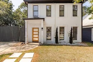 Une maison à deux étages avec une porte d’entrée, un petit porche et une cour clôturée.