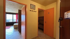 A hallway with a bed in the background, a door with a sign, and a window with curtains.