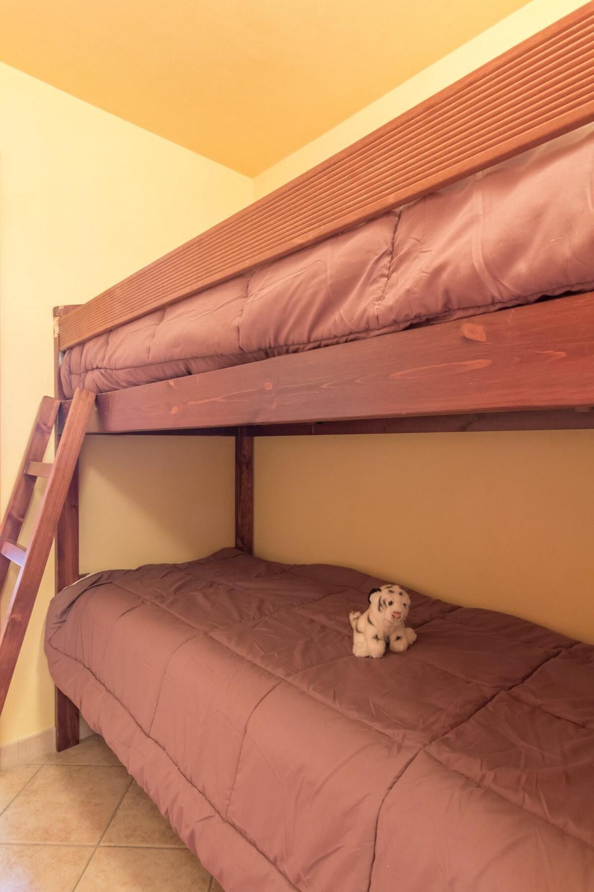 A bunk bed with a wooden ladder, a plush dog toy, and a tiled floor.