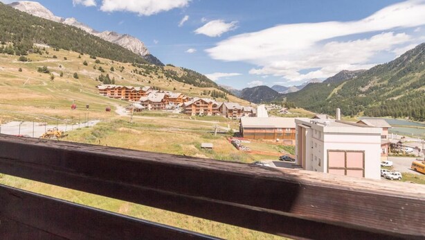 A mountain resort with chalet-style buildings, a parking area, and a view of the surrounding mountains.