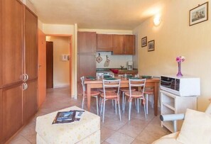 Cozinha compacta com armários de madeira, uma mesa de jantar com cadeiras, geladeira e micro-ondas.