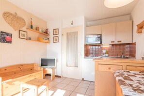 Un ambiente compatto con angolo cottura, una panca in legno, una televisione e un accesso a un bagno.