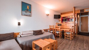A cozy room with a sofa, a wooden table, and a kitchen area with a microwave and a television.