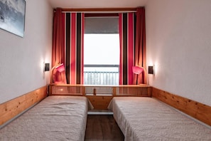 Une petite pièce agréable et chaleureuse, avec deux lits, une fenêtre ornée de rideaux à rayures et deux lampes fixées au mur.