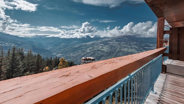 A balcony with a wooden railing overlooking a mountainous landscape.