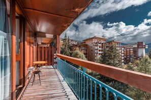 A balcony with a wooden table and chairs, overlooking a mountainous area with buildings.