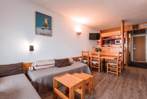 A cozy room with a sofa, a wooden table, and a kitchen area with a microwave and a television.