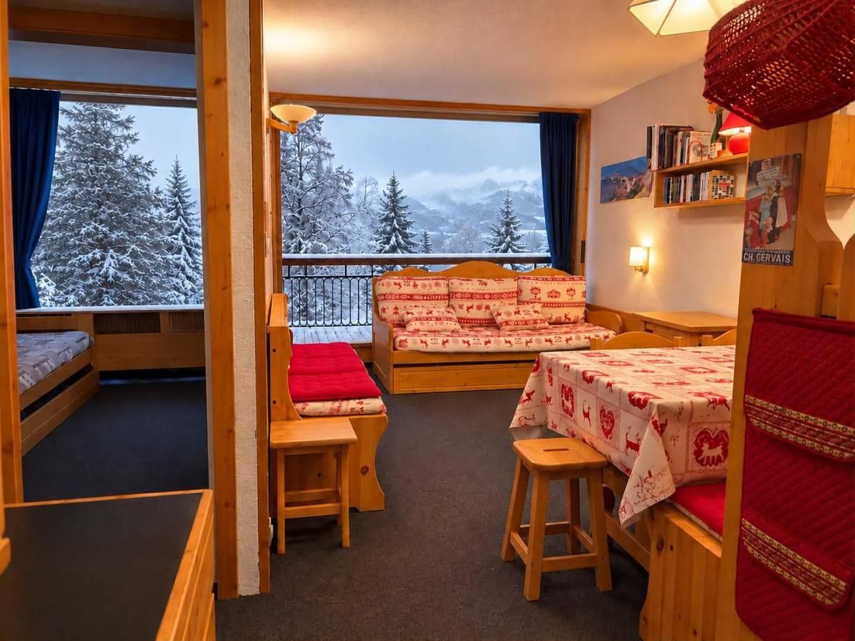 A cozy room with a bed, a table, and a bench. There is a window with a view of snow-covered trees.