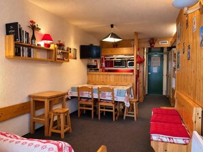 A compact room with a dining table, chairs, a television, and a kitchenette.