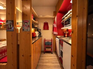 A narrow kitchen with wooden cabinets, a red wall, and a small cart. - 1st floor, view valley, tv, 40m², Les Arcs (Les Arcs)