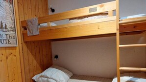 En køjeseng med træramme, en enkeltseng for neden og en stige på højre side.