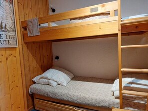 Un lit superposé avec une structure en bois, un lit simple en bas et une échelle sur le côté droit.