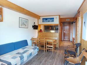 A cozy living room with a blue sofa, wooden dining table, and chairs. A kitchen area is visible in the background with a microwave and a sink. - 11st floor, view valley, balcony, tv, 40m², Les Arcs (Les Arcs)