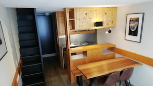 Une cuisine de taille réduite, dotée de meubles en bois, d’une table à manger et d’un escalier menant à une autre pièce.