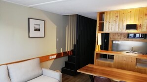 Un espace de vie compact comprenant un canapé, une table à manger en bois avec des chaises, un coin cuisine avec un four à micro-ondes et un escalier.