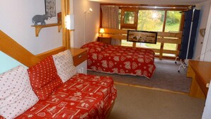 Een kamer met twee bedden, elk voorzien van rode beddengoed en witte kussens, een houten bureau, een stoel en een raam met uitzicht op groen.