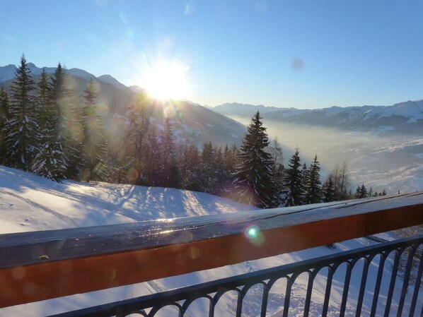 A snowy mountain landscape with a clear sky and the sun shining through the trees.