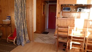Interior em madeira com área de refeições, cozinha com micro-ondas e uma porta vermelha que dá para outro cômodo.