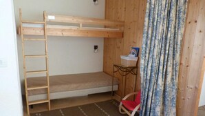 Quarto com beliche, uma pequena escrivaninha, cadeira e cortina estampada.