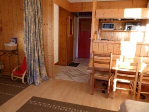 A wooden interior with a dining area, a kitchen with a microwave, and a red door leading to another room.
