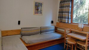 Habitación compacta con sofá cama, una mesita y ventana con cortinas.
