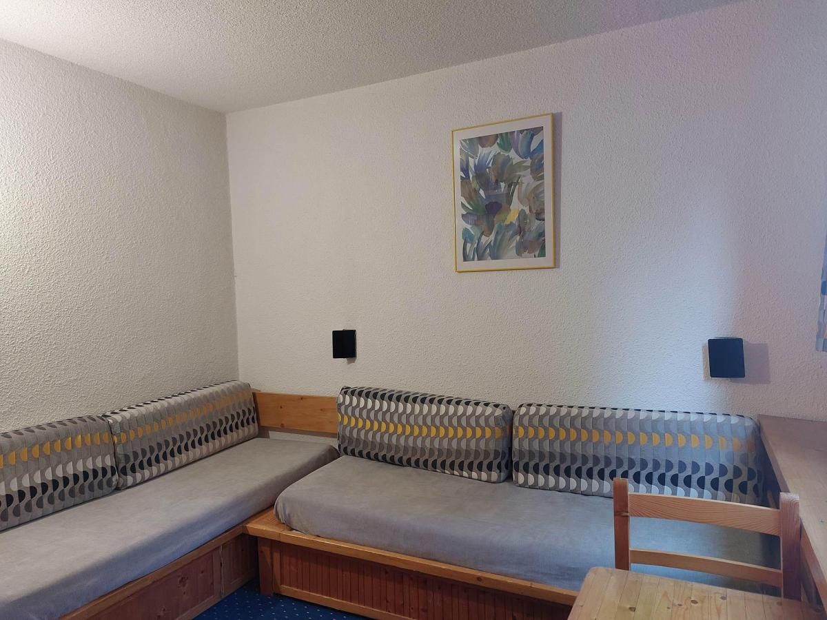 Et værelse med en sofa op ad en hvid væg, et indrammet abstrakt maleri og to små sorte højttalere.