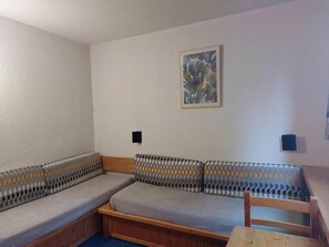 A room with a sofa set against a white wall, a framed abstract painting, and two small black speakers.
