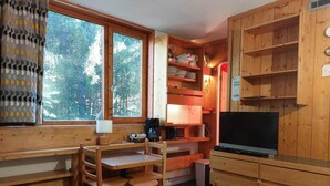 Una habitación acogedora tipo cabaña con un escritorio de madera, sillas, un televisor y una estantería.