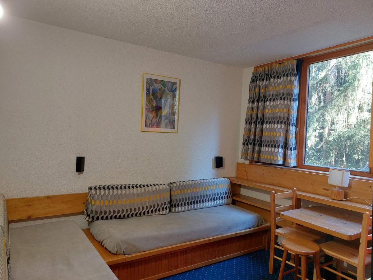 A compact room with a sofa bed, a small table, and a window with curtains.