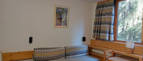 A compact room with a sofa bed, a small table, and a window with curtains.