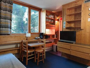 A cozy cabin room with a wooden desk, chairs, a television, and a bookshelf.