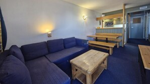 Un espacio habitable funcional con sofá, mesas de madera y una pequeña cocina.