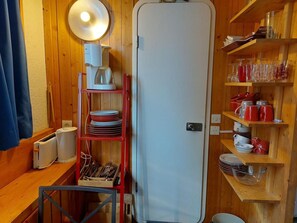 A compact kitchen with wooden walls, a white refrigerator, a red shelf unit with dishes, and a coffee maker. - 9th floor, view firs, tv, 17m², Les Arcs (Les Arcs)