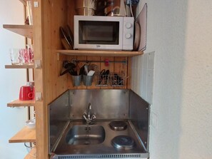 A compact kitchen with a microwave, sink, and wooden shelves. - 9th floor, view firs, tv, 17m², Les Arcs (Les Arcs)