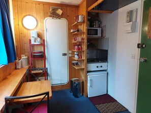 A compact kitchen with wooden walls, a white refrigerator, a microwave, and a small stove. There is a wooden shelf with dishes and a trash bin. - 9th floor, view firs, tv, 17m², Les Arcs (Les Arcs)