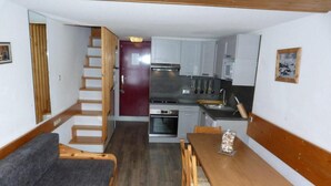 Un espacio habitable compacto con una escalera de madera, una zona de comedor con mesa y sillas, y una kitchenette equipada con electrodomésticos modernos.
