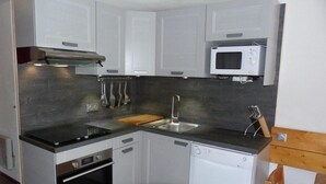 Cocina compacta con armarios blancos, encimera negra, horno integrado, lavavajillas y microondas.