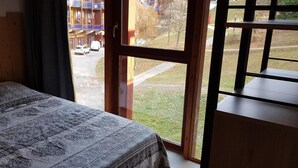Un dormitorio con cama, ventana y vista a un edificio y una calle.