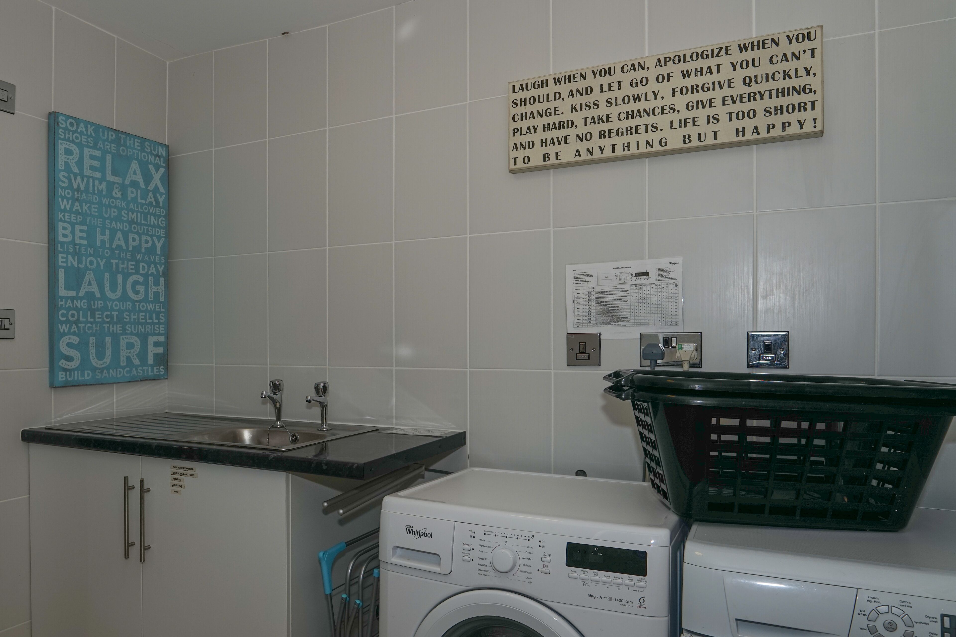 Un lavadero con lavadora y secadora Whirlpool, un lavabo y un cartel con frases motivadoras.